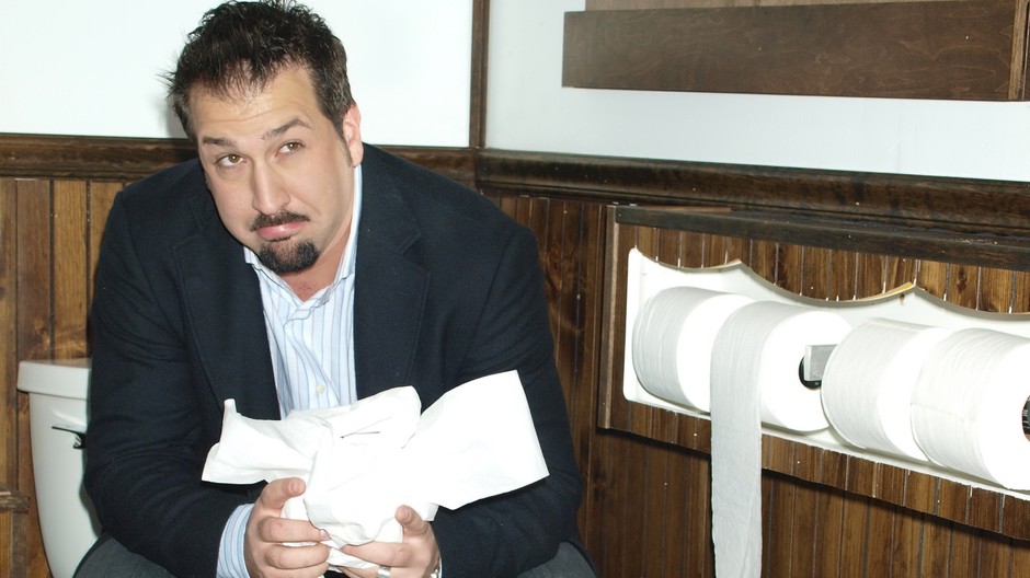 Muž sedí na toalete s rolkami toaletného papieru v rukách